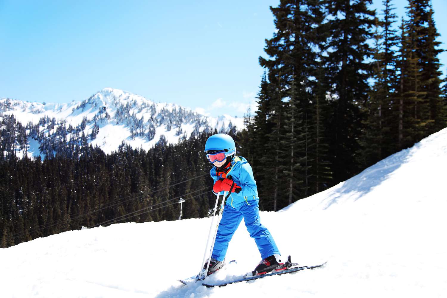 Enfant skiant en descente à Crystal Mountain Resort, Washington, avec en toile de fond des sapins et des sommets enneigés