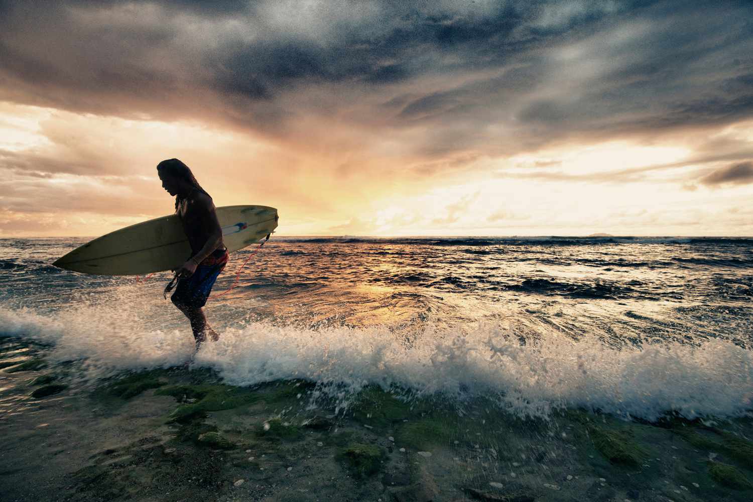 Surfer sortant de l'eau avec sa planche de surf au coucher du soleil à Rincon, Porto Rico