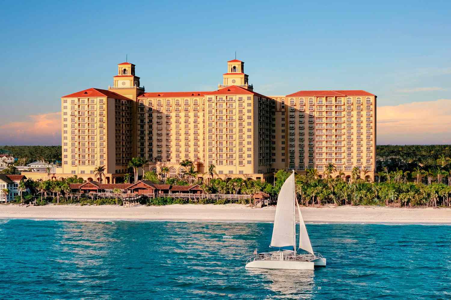 Vue extérieure du Ritz-Carlton Naples avec l'océan et la plage au premier plan alors qu'un bateau passe