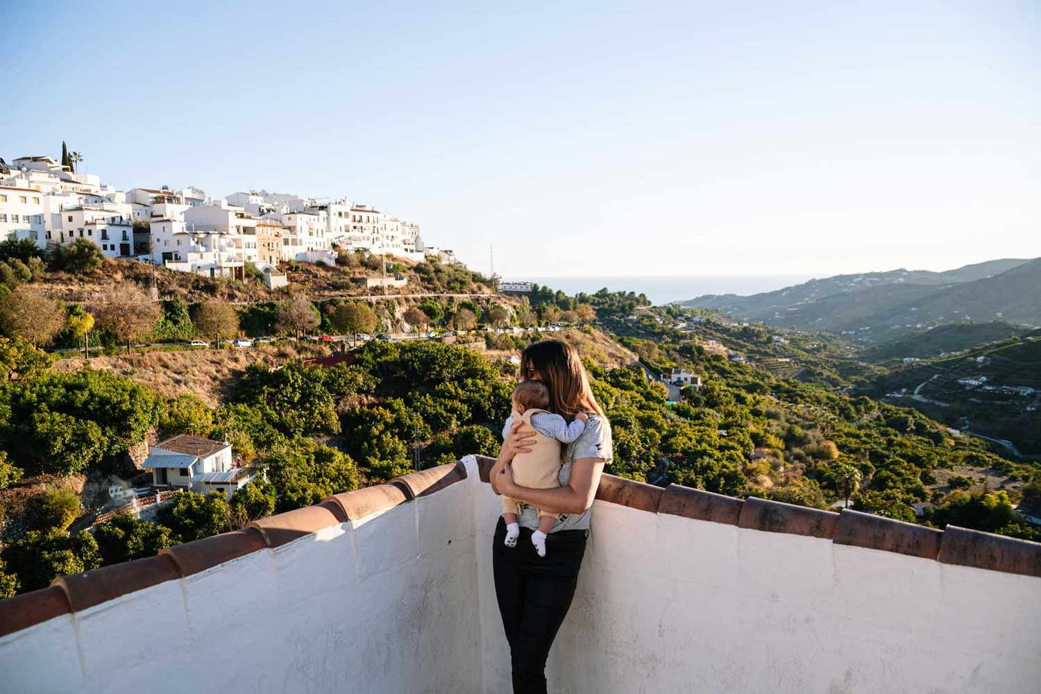 Portrait d'une jeune mère tenant son bébé. Village andalou avec des maisons blanches et la côte en arrière-plan.