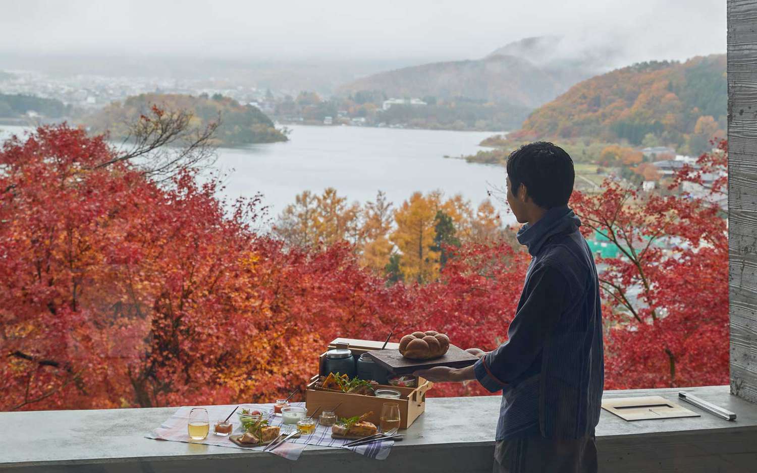 Un homme se tient devant un feuillage d'automne rouge vif depuis une terrasse au complexe Hoshinoya Fuji