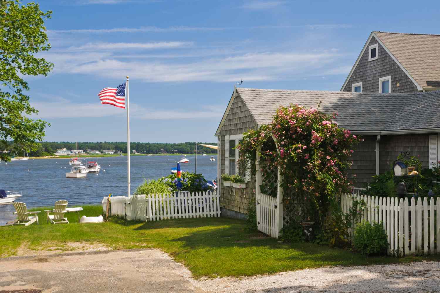 Un cottage en bord de mer dans une tranquille crique à Cape Cod dispose d'une porte en arc couverte de roses.