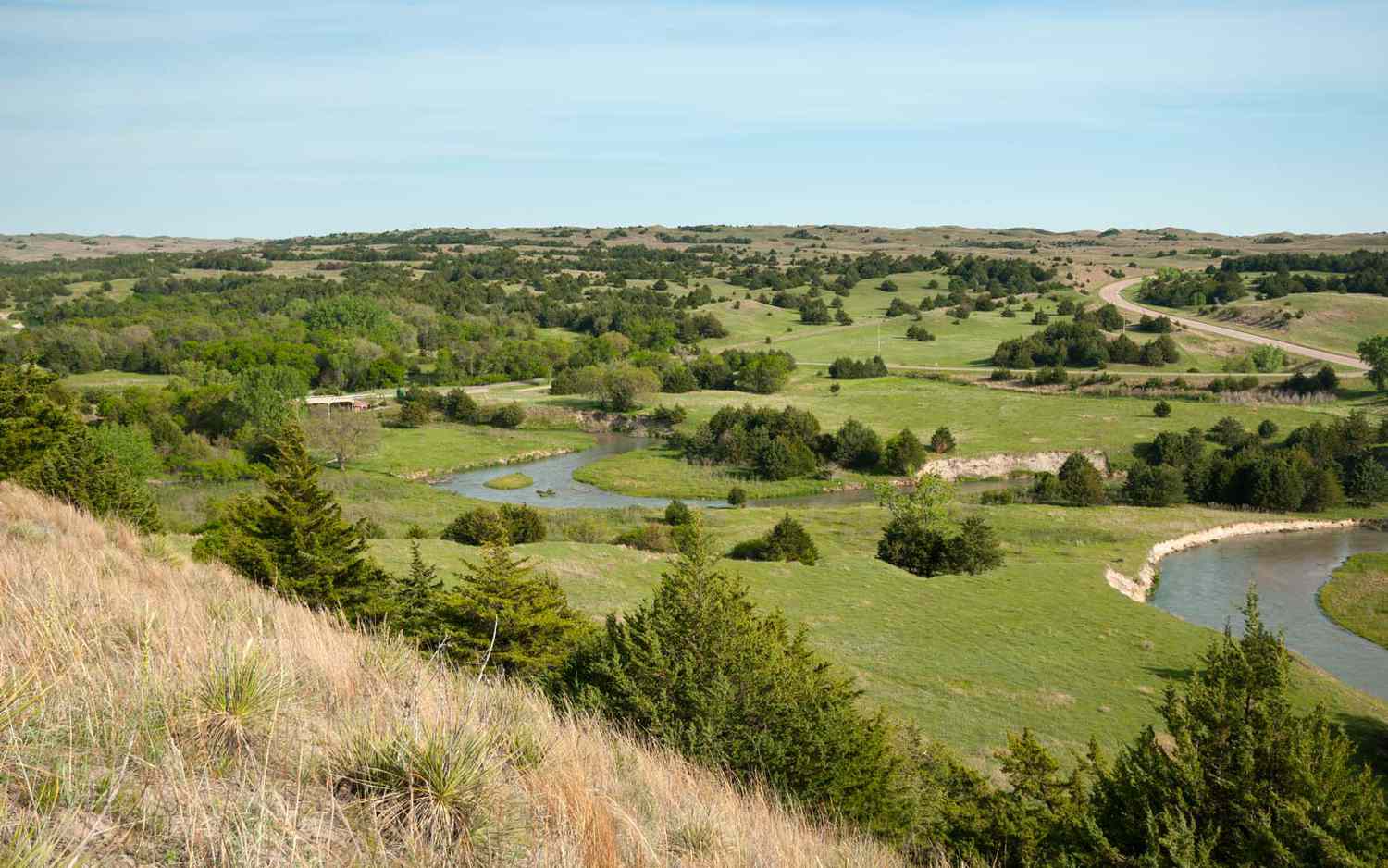 A winding stream cuts through the grassy, tree-covered hills of Nebraska's Valentine National Wildlife Refuge