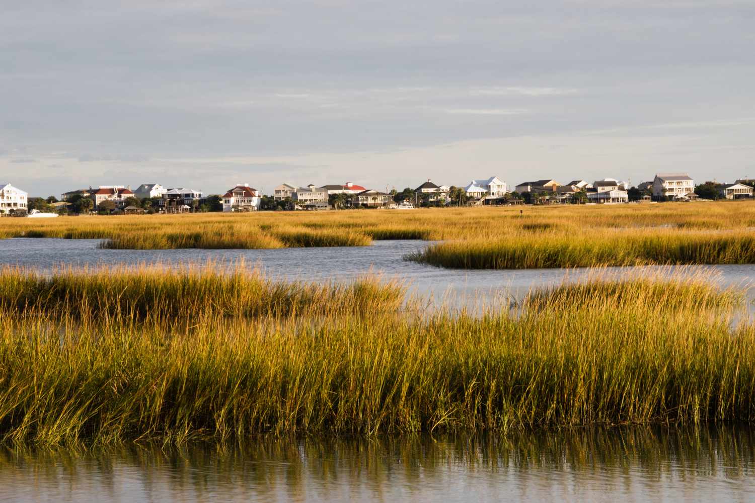 Le soleil se couche sur un marais d'eau salée à Murrells Inlet, Caroline du Sud. L'accent de l'appareil photo est mis sur le marais et non sur les maisons qui bordent le bord de l'eau en arrière-plan.