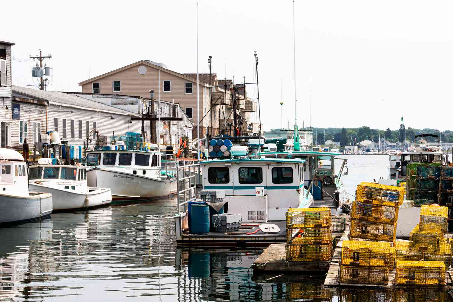 Bateaux de pêche commerciaux amarrés dans un canal avec des cages à homard colorées empilées sur le quai derrière des bâtiments.