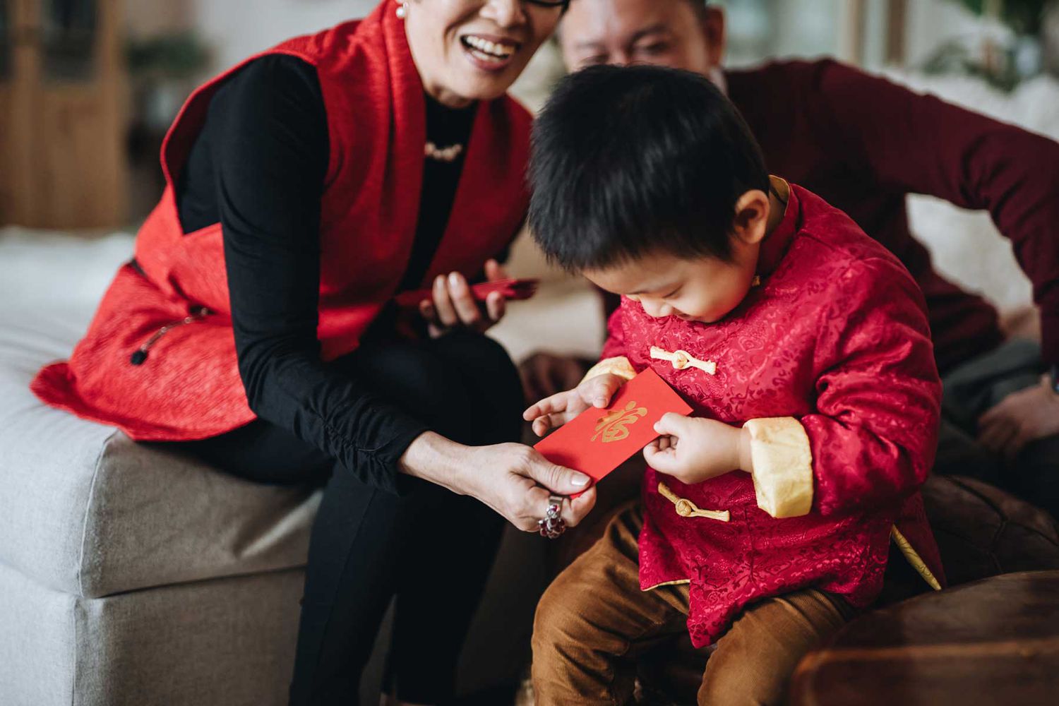 Un petit-fils habillé en costume traditionnel chinois rouge reçoit des enveloppes rouges (lai see) des mains de ses grands-parents avec joie pour le Nouvel An chinois