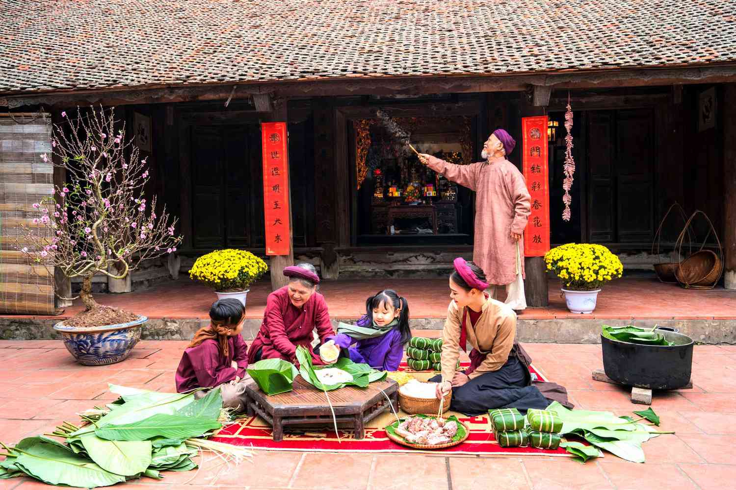 Des membres de la famille vietnamienne préparant ensemble des Banh Chung dans la cour d'une maison au style ancien. Le gâteau Chung est un plat très connu qui ne peut manquer sur l'autel et lors du repas familial des Vietnamiens pendant la fête de Têt.