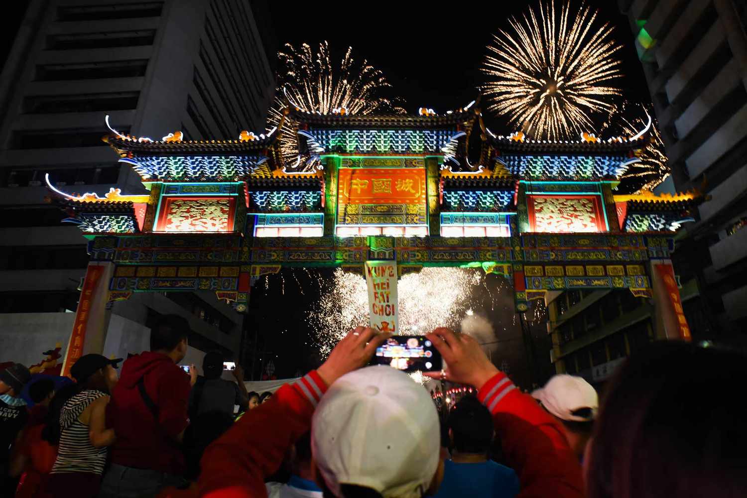 Un homme filme la scène avec son téléphone portable alors que des feux d'artifice illuminent le ciel au-dessus de l'arc de l'amitié de Chinatown, le plus grand au monde, situé dans le quartier de Binondo, le Chinatown de Manille, lors de la veille du Nouvel An chinois, à Manille, aux Philippines.